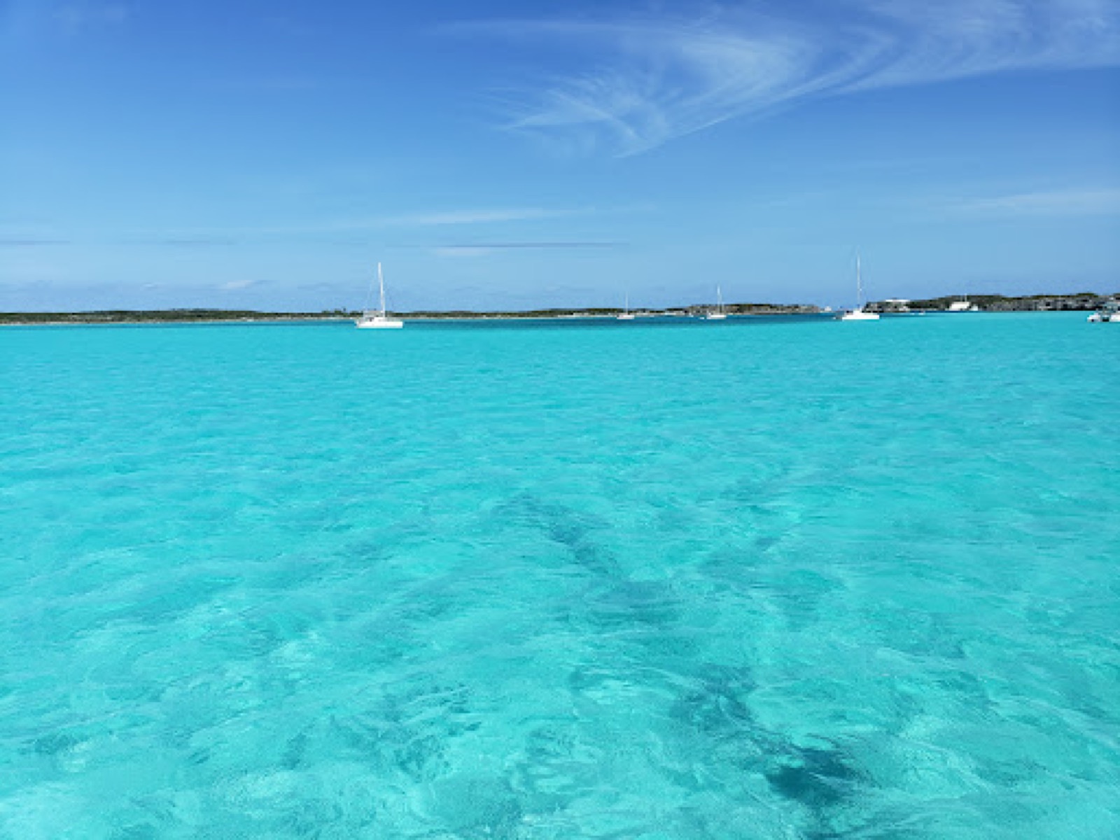 Sailboats anchored in shallow turquoise water off a cay in the Exumas