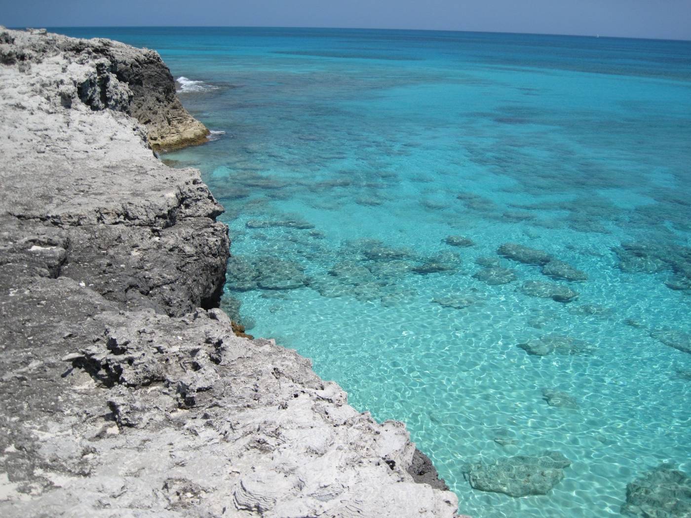 Pale limestone cliff edge above clear turquoise shallows and reef patches